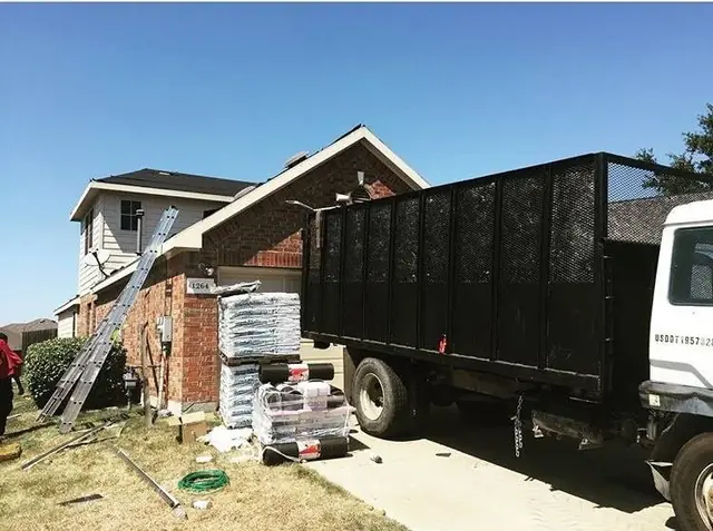 Shingle bundles staged and a dump trailer on the driveway at the start of a MAG Builders tear-off